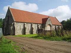 Long stone building with buttressed walls and red tiled roof.