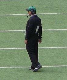 A horizontal photograph of a man standing on a football field