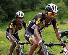 Two dark-skinned men riding bicycles.