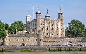 A keep seen from a river, rising behind a gate. The keep is large, square in plan, and has four corner towers, three square and one round, all topped by lead cupolas