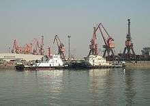 two black and white tugboats berthed against a background of large cranes