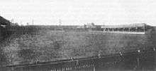 Grass football pitch with a small covered stand on the right hand side.