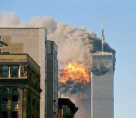 Two tall, gray, rectangular buildings spewing black smoke and flames, particularly from the left of the two.