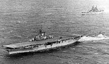 A black and white photo of an aircraft carrier and a battleship in the background.