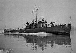 The USS PC-815, a single-masted vessel running at speed with a large wake, and with a deck gun prominent on the bow