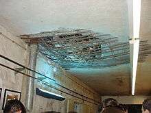 A concrete ceiling with a large hole punched through, exposing the reinforcing metal rods embedded in the concrete