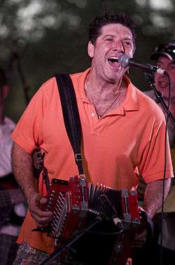 Wayne Toups singing into the microphone and playing the accordion.