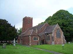 Red stone building with square tower. In the foreground are gravestones.