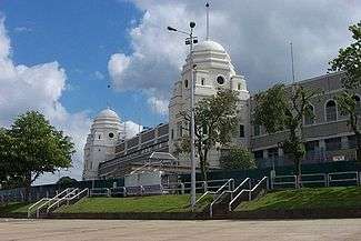 A stadium on a sunny day, two large white towers can be seen with one either side of the entrance.