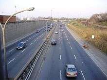 8-lane roadway from an overhead bridge with parallel 3 lines of train tracks on the right