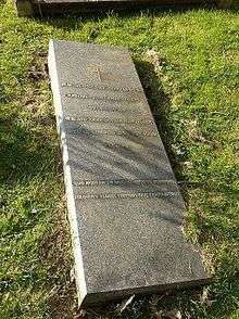 A horizontal gravestone of polished granite, partially sunk on one side