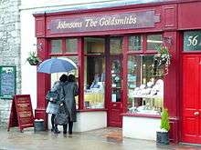 Women peer through a shop window on a rainy day