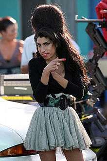 Knee high portrait of woman in her twenties wearing a short gathered skirt, light grey dress and dark cardigan