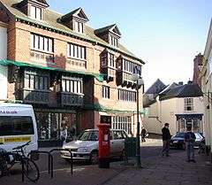 Street scene with buildings and shops. The three-storey building on the left has a sign saying The Courthouse.