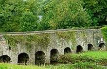 A low, stone arch bridge with eight consecutive arches in view.