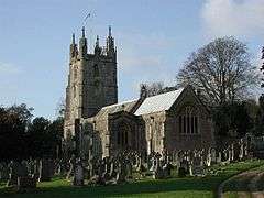 Stone building with square tower. In the foreground are gravestones.